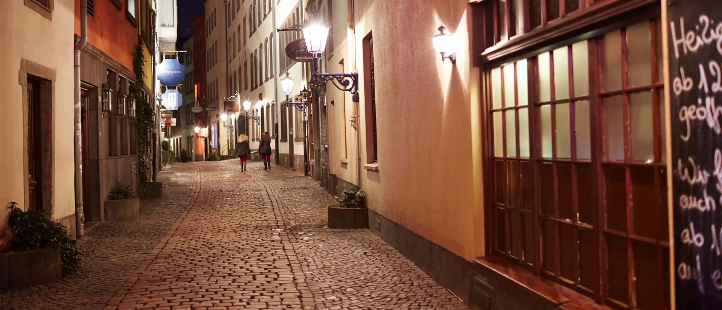 Kölner Altstadt Abendstimmung in einer Altstadtgasse von Köln, belebt von zwei Personen auf Kopfsteinpflaster.