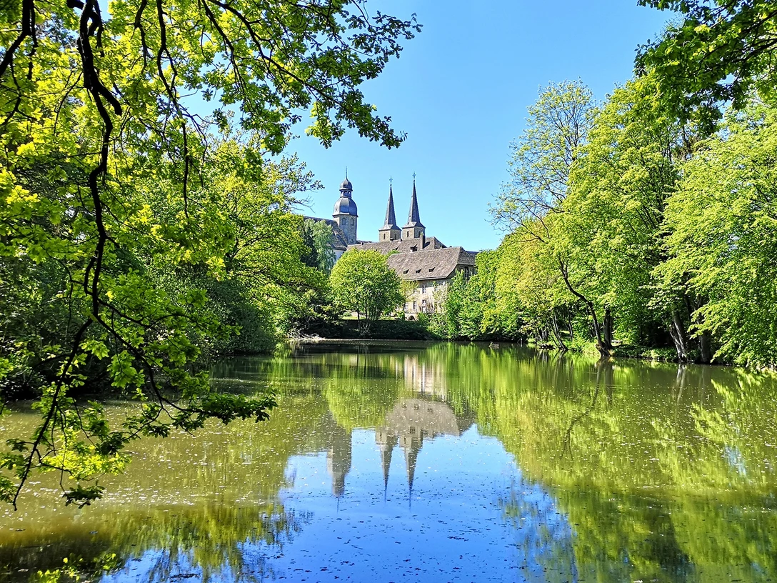 Abtei Marienmünster mit ihren markanten Türmen spiegelt sich in einem stillen, umgebenen Teich.