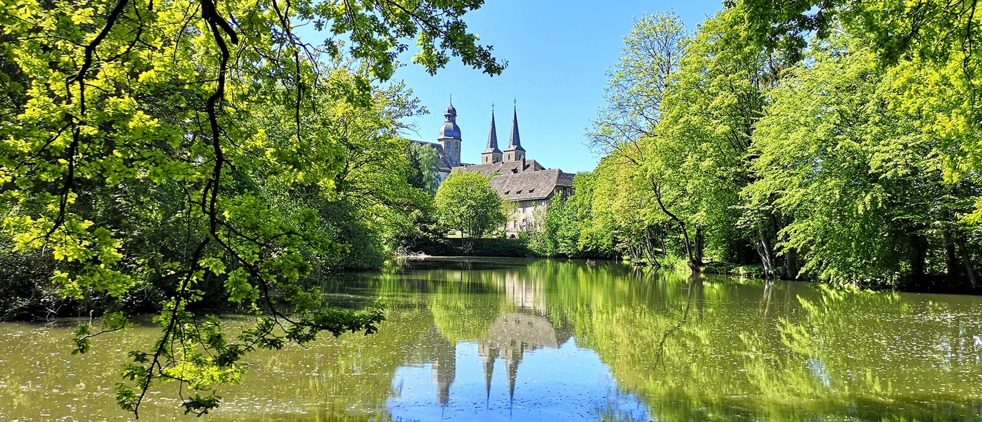 Abtei Marienmünster mit ihren markanten Türmen spiegelt sich in einem stillen, umgebenen Teich.