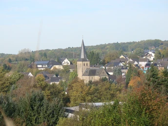 Blick auf Ruppichteroth <p>Kirchturm in Ruppichteroth umgeben von Bäumen und Häusern, Panorama mit bewaldetem Hintergrund.</p>