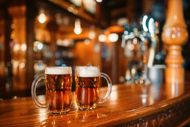 Two beer mugs on wooden bar counter, macro, nobody. Octoberfest symbol or concept. Glasses with golden beverage and foam on the table in pub, closeup view, blur background Two beer mugs on wooden bar counter, macro, nobody. Octoberfest symbol or concept. Glasses with golden beverage and foam on the table in pub, closeup view, blur background