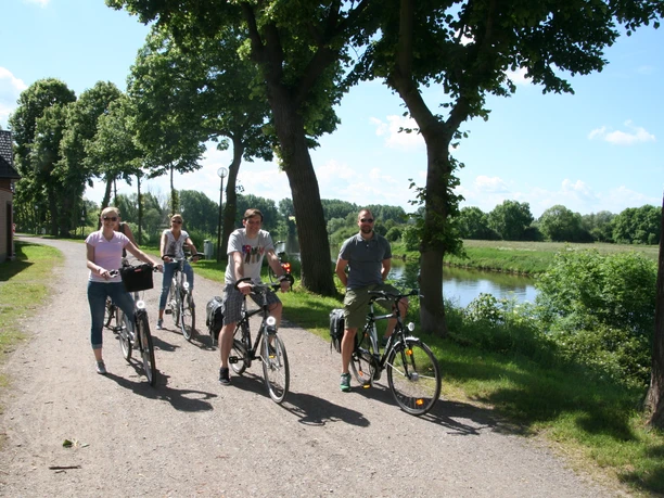 Radler Nienburg Vier Radfahrer auf einem Schotterweg entlang eines Flusses, umgeben von üppigem Grün und Bäumen.