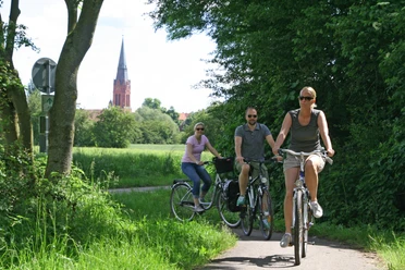 Radler bei Nienburg Cyclists on a shady path near Nienburg, in the background a church with a striking tower.