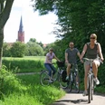 Radler bei Nienburg Radfahrer auf einem schattigen Weg nahe Nienburg, im Hintergrund eine Kirche mit markantem Turm.