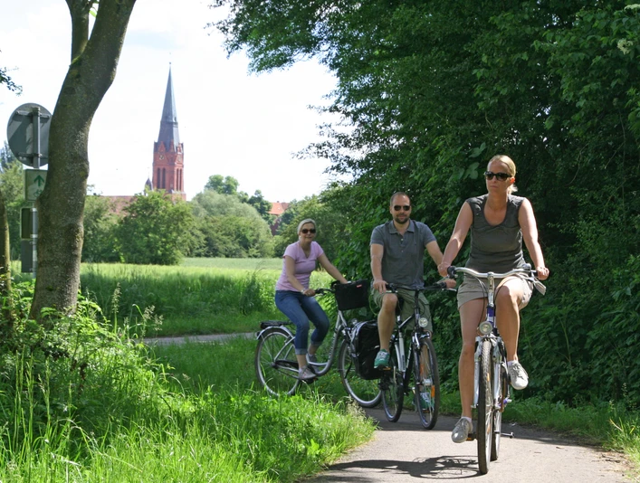 Radler bei Nienburg Radfahrer auf einem schattigen Weg nahe Nienburg, im Hintergrund eine Kirche mit markantem Turm.Cyclists on a shady path near Nienburg, in the background a church with a striking tower.Cyklister på en skyggefuld sti nær Nienburg, i baggrunden en kirke med et markant tårn.Fietsers op een schaduwrijk pad bij Nienburg, op de achtergrond een kerk met een opvallende toren.