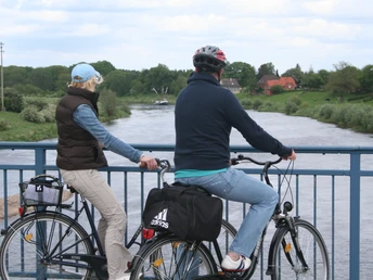 Two cyclists stand on a bridge and look out over the idyllic course of the Weser.