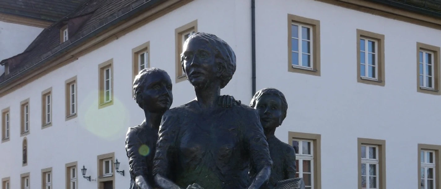 Denkmal Zigarrendreherinnen Bronzefiguren dreier Frauen, Symbol für die Zigarrendreherinnen, auf einem Sockel vor einem Gebäude.