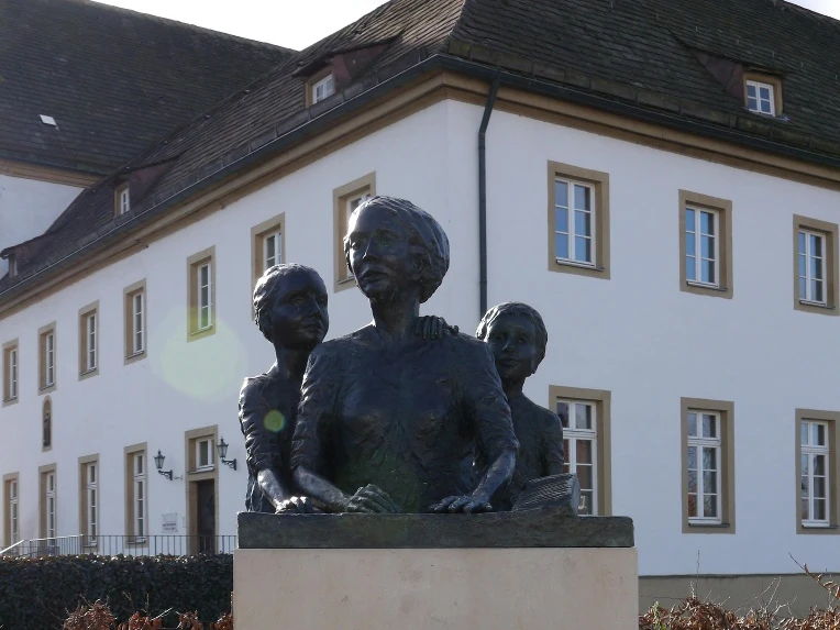 Denkmal Zigarrendreherinnen Bronzefiguren dreier Frauen, Symbol für die Zigarrendreherinnen, auf einem Sockel vor einem Gebäude.