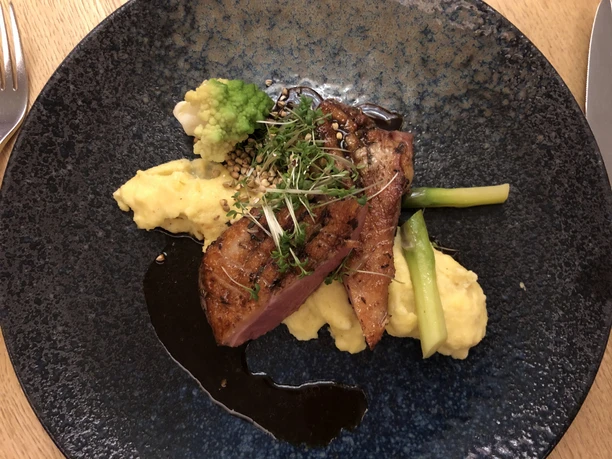 Duck breast on mashed potatoes with green asparagus spears and romanesco on a blue plate.