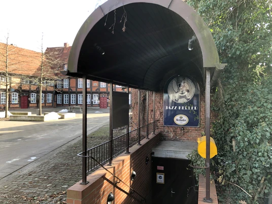 Eingang des Jazz Kellers Nienburg mit gewölbtem Dach und Treppe, umgeben von Backsteingebäuden.