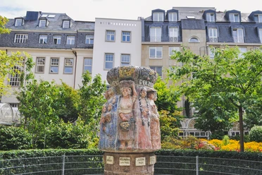 Women's fountain The Frauenbrunnen fountain shows ten life-size female figures "the women of Cologne through the ages", surrounded by lush greenery against an urban backdrop.