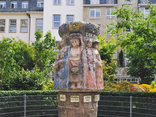 Women's fountain Der Frauenbrunnen zeigt detailreich gestaltete weibliche Figuren in traditioneller Tracht, umgeben von Natur und historischen Gebäuden.The women's fountain shows detailed female figures in traditional costume, surrounded by nature and historic buildings.