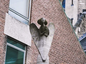 Engelsstatue Eine Engelsstatue aus Stein erhebt sich majestätisch an einem Gebäude aus roten Backsteinen.