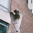 Engelsstatue Eine Engelsstatue aus Stein erhebt sich majestätisch an einem Gebäude aus roten Backsteinen.A stone statue of an angel rises majestically from a red brick building.