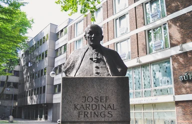 Joseph Frings Monument The Joseph Frings monument shows a bronze bust of the cardinal on a stone plinth, surrounded by modern views of buildings.