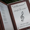 Willkommensschild der "Straße der Lieder" mit Notenschlüssel und Gedicht, inspiriert zum Mitsingen.