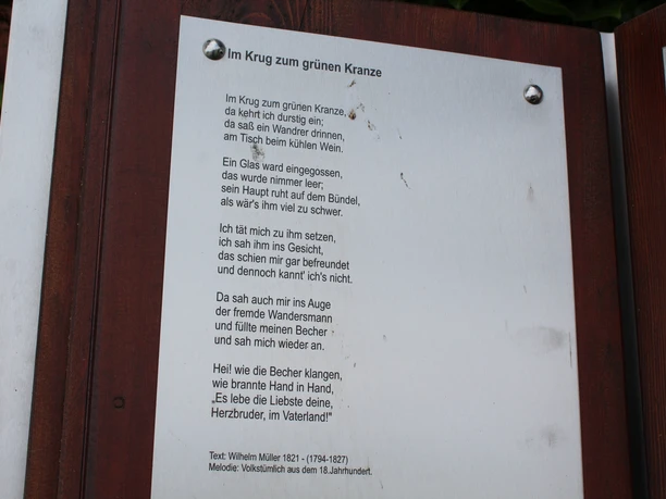 A plaque featuring the poem "Im Krug zum grünen Kranze" by Wilhelm Müller, accompanied by sheet music.