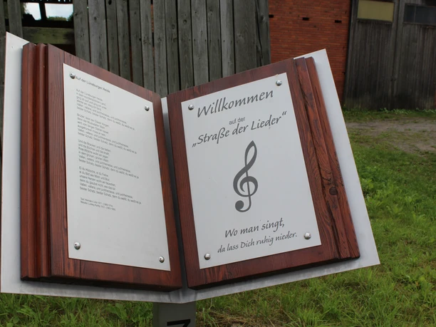 Straße der Lieder Marklohe Ein hölzernes Schild mit dem Text "Willkommen auf der Straße der Lieder" und einer Musiknote.