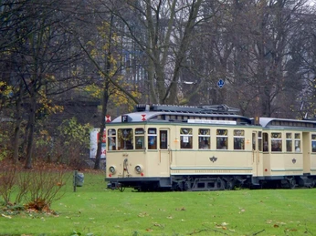 Thielenbruch Tram Museum Die historische Straßenbahn in cremefarbenem Design fährt durch eine parkähnliche Umgebung an einem bewölkten Tag.The historic streetcar in cream-colored design travels through a park-like setting on a cloudy day.