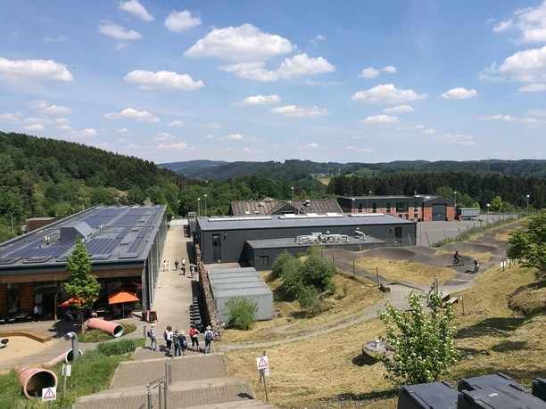 Blick auf :metabolon <p>Landschaft mit modernem Gebäude, Solarpanels und Hügeln unter blauem Himmel mit Wolken.</p>