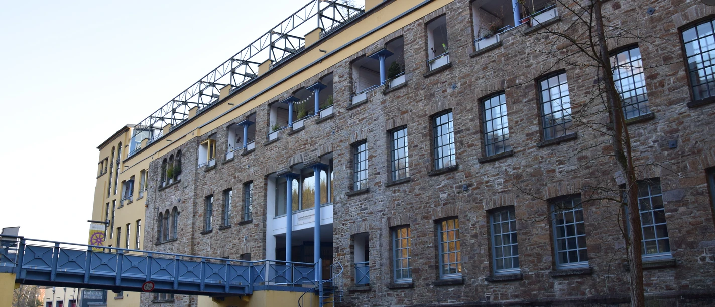 Historisches, mehrstöckiges Gebäude mit Natursteinfassade und blauen Brückenüberwegungen im Vordergrund.