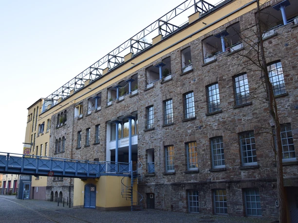 Industriemuseum Engelskirchen Historisches, mehrstöckiges Gebäude mit Natursteinfassade und blauen Brückenüberwegungen im Vordergrund.