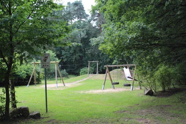 SG Steimbke - Waldspielplatz Stöckse Waldspielplatz mit Schaukel, Rutsche und Schlitten im Grünen, umgeben von hohen Bäumen und Wiesen.
