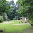 SG Steimbke - Waldspielplatz Stöckse Waldspielplatz mit Schaukel, Rutsche und Schlitten im Grünen, umgeben von hohen Bäumen und Wiesen.