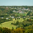 Lohmar-Wahlscheid Weitläufige Landschaft mit sanften Hügeln, grünen Wiesen und einer kleinen Siedlung am Horizont.