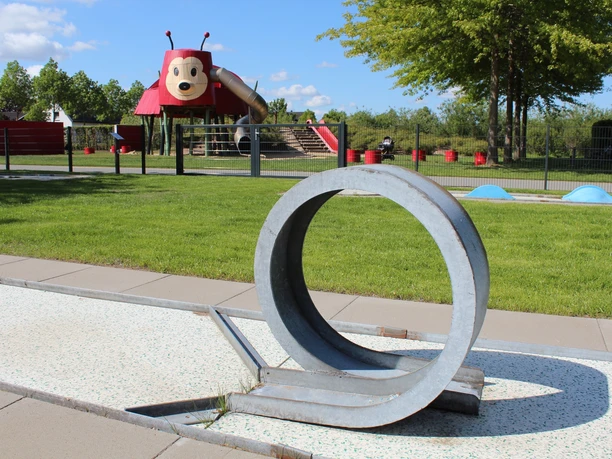 Spielplatz mit Marienkäfer-Themenrutsche, Rasenflächen und modernem Kunst-Spielgerät im Vordergrund.