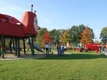 Ein farbenfroher Spielplatz mit einem großen Marienkäfer-Klettergerüst und fröhlichen spielenden Kindern.