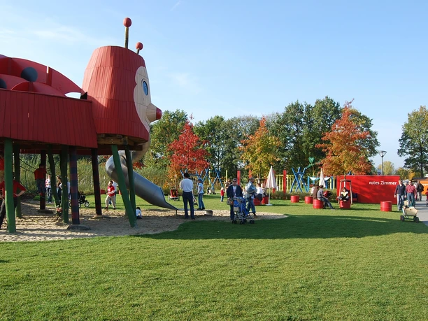 Ein farbenfroher Spielplatz mit einem großen Marienkäfer-Klettergerüst und fröhlichen spielenden Kindern.