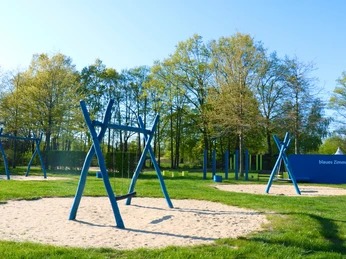 Blaues Spielzimmer Ein Spielplatz im Freien mit mehreren blauen Schaukeln und Klettergeräten auf Sandflächen.