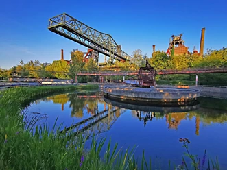 <p>Industrieanlage im Landschaftspark Duisburg-Nord mit Wasserbecken, blauer Himmel und grüner Natur.</p>
