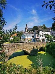 RevierRoute GartenStadt.jpg <p>Historische Steinbrücke über grün schimmerndem Wasser, dahinter Fachwerkhäuser und ein Kirchturm.</p>
