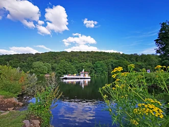 RevierRoute Von Ruhr zur Ruhr.jpg <p>Ein weißes Ausflugsschiff auf einem ruhigen Fluss, umgeben von grünen Bäumen und bunten Blumen.</p>