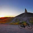 RevierRoute Haldenglück.jpg Ein einsames Fahrrad steht bei Sonnenuntergang vor einer Haldenlandschaft mit einem markanten Gipfelbau.