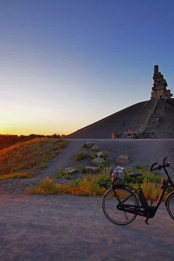 RevierRoute Haldenglück.jpg Ein einsames Fahrrad steht bei Sonnenuntergang vor einer Haldenlandschaft mit einem markanten Gipfelbau.