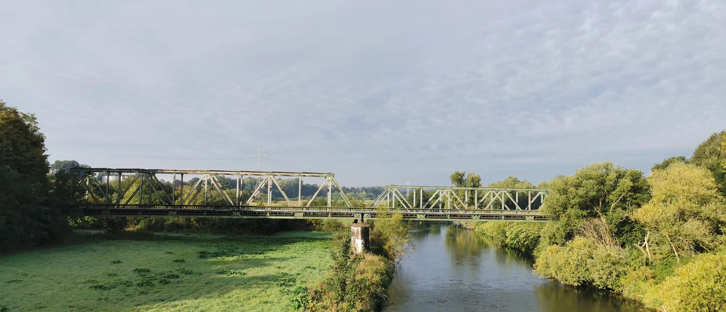 RevierRoute Handelswege Stahlbahnbrücke über einem Fluss, umgeben von grüner Landschaft und klarem Himmel.