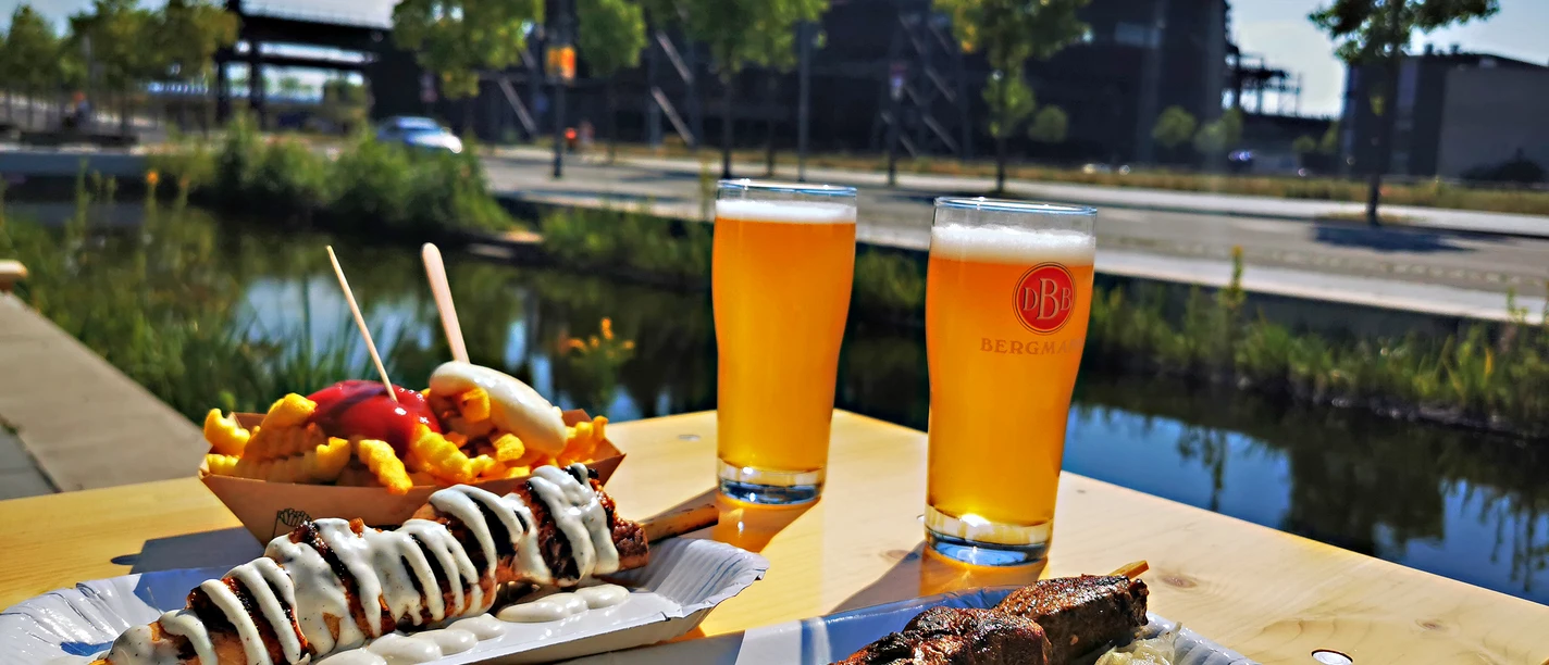 RevierRoute RevierWasser.jpg <p>Grillspieße, Pommes und Bier an einem sonnigen Tisch vor einem Industriebau.</p>