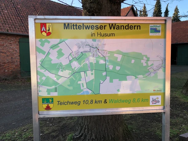 Wandelroutebord in Husum met kaart en afstandsinformatie: Teichweg 10.8 km, Waldweg 8.6 km.
