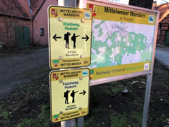 Wegweiser für Wanderwege in Husum, mit Kartenansicht und Entfernungsangaben für Teich- und Waldweg.Signpost for hiking trails in Husum, with map view and distance information for pond and forest trail.Skilt til vandrestier i Husum, med kortvisning og afstandsinformation til sø og skovsti.Wegwijzer voor wandelroutes in Husum, met kaartweergave en afstandsinformatie voor vijver- en bospad.