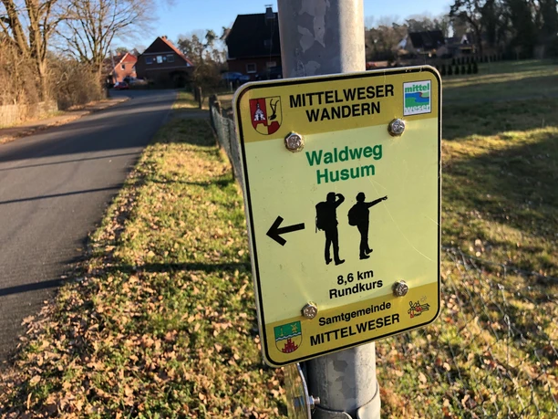 Schild Waldweg Husum Wegweiser zeigt die Richtung zum Waldweg Husum und weist auf einen 8,6 km langen Rundkurs hin.