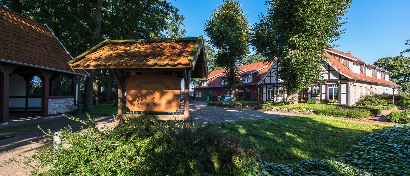 Bioland Hof Vaal Eingangsbereich des Bioland-Hofs Vaal mit Hofschild, Fachwerkgebäuden und grünen Bäumen im Sonnenschein.