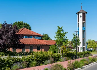 Ev.-luth. Gemeindezentrum Backsteinkirche mit achteckigem Dach und modernem Glockenturm neben bepflanztem Vorplatz