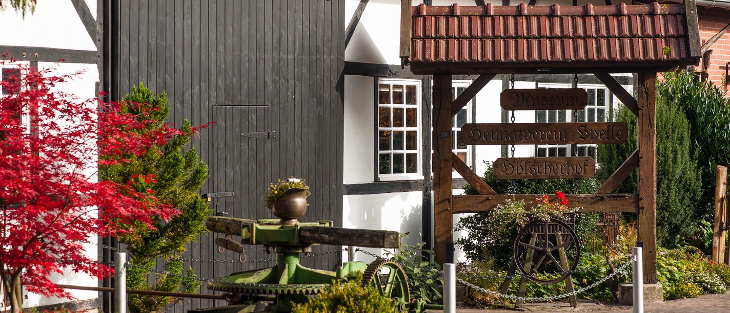 Museumsscheune „Hölscherhof“ Holzbeschilderter Eingang zur Museumsscheune Hölscherhof mit Fachwerkfassade und Gartenpflanzen