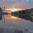 Duisburg Innenhafen Abendstimmung.JPG <p>Sonnenuntergang spiegelt sich im ruhigen Wasser eines Hafenbeckens, umgeben von Gebäuden und Kränen.</p>