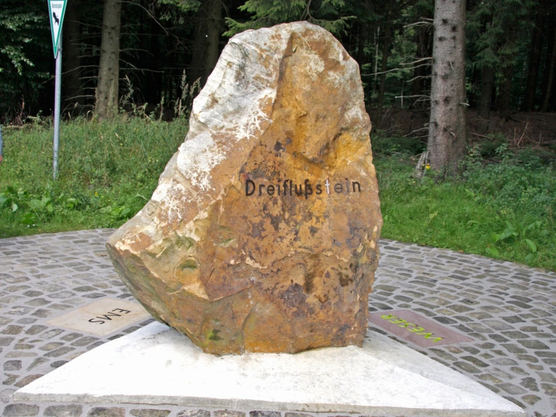 Dreiflussstein Großer Felsen in Waldgebiet markiert mit "Dreiflussstein", zeigt Richtungen zu Weser, Eder und Rhein.