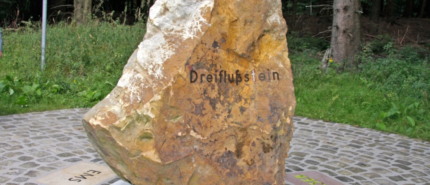 Dreiflussstein Großer Felsen in Waldgebiet markiert mit "Dreiflussstein", zeigt Richtungen zu Weser, Eder und Rhein.