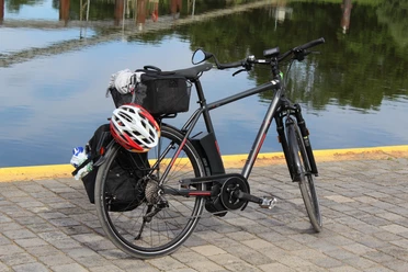 Rad Mittelweser Ein schwarzes Fahrrad mit Gepäckträger und Helm steht auf gepflastertem Boden vor ruhigem Wasser.